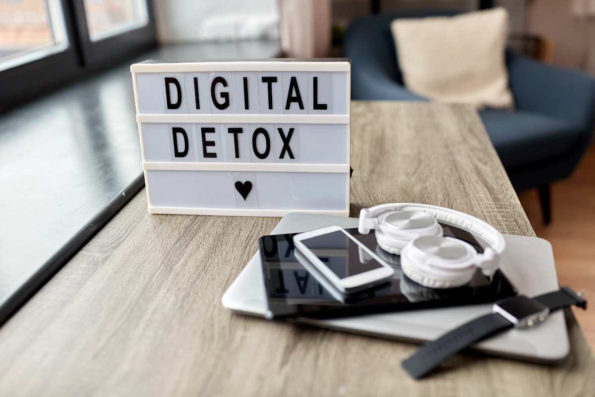 Placa com a frase "Digital Detox" ao lado de fones, celular e smartwatch sobre uma mesa