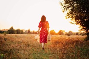Mulher caminhando por um campo ao entardecer com chapéu e cesta nas mãos