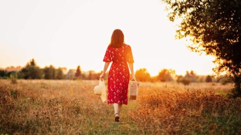 Mulher caminhando por um campo ao entardecer com chapéu e cesta nas mãos